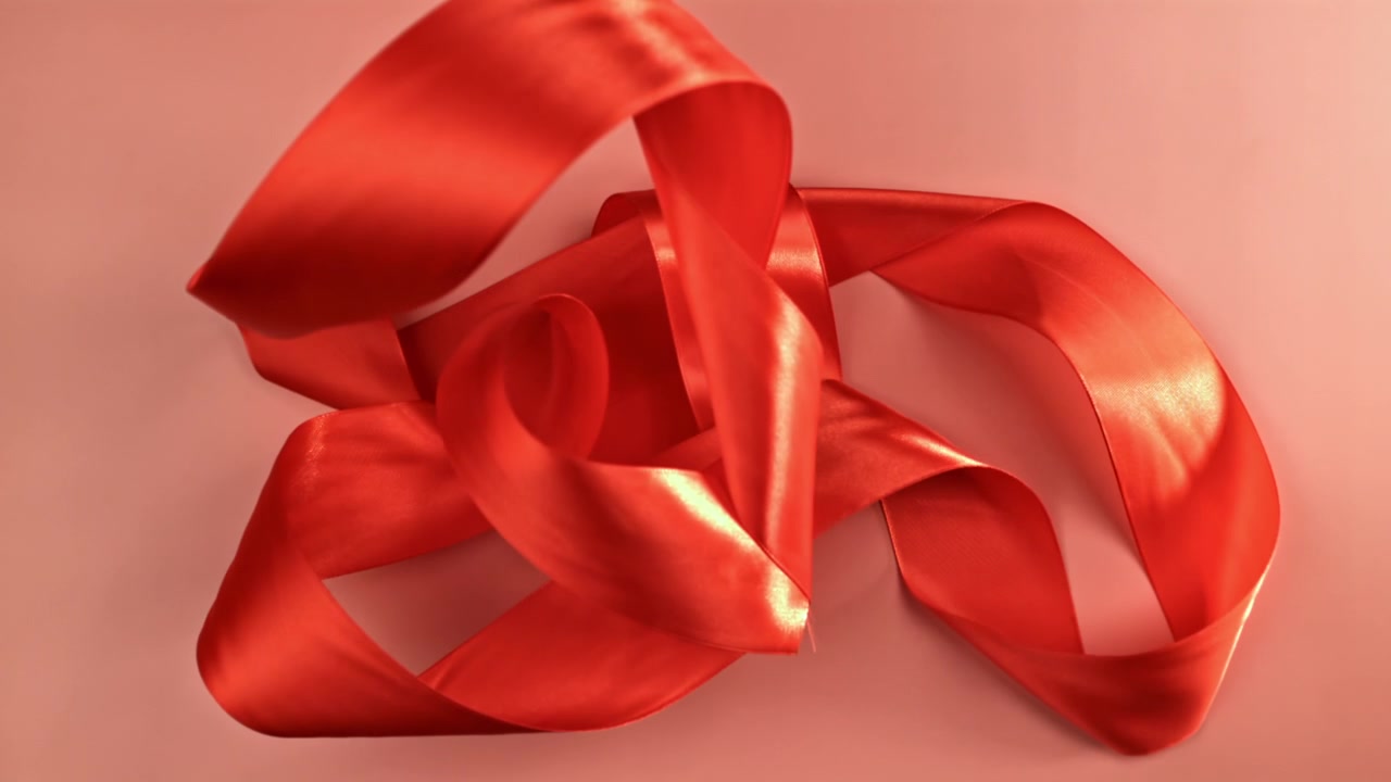 Rotes Satinband fällt und legt sich auf rosa Hintergrund.