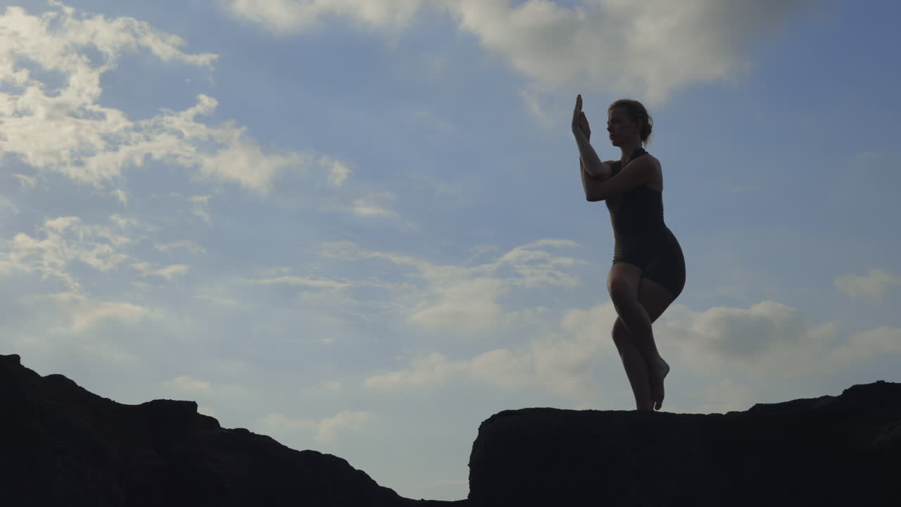 Woman practicing yoga on a cliff