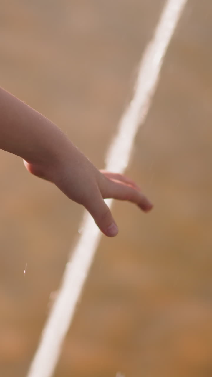 Little girl hand touches powerful fountain water jet on city street close view slow motion. Refreshing during hot summer day. Child enjoys splashing water