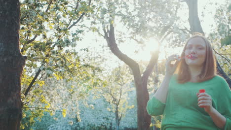 happy pregnant woman blowing bubbles in bloomy park