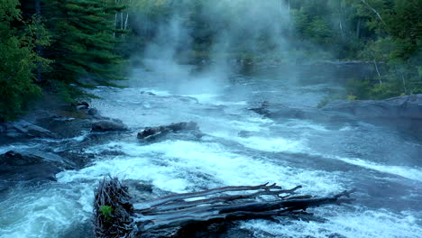 aerial drone shot over the dark misty forest stream at big wilson falls with logs in the waterfall at dusk in maine