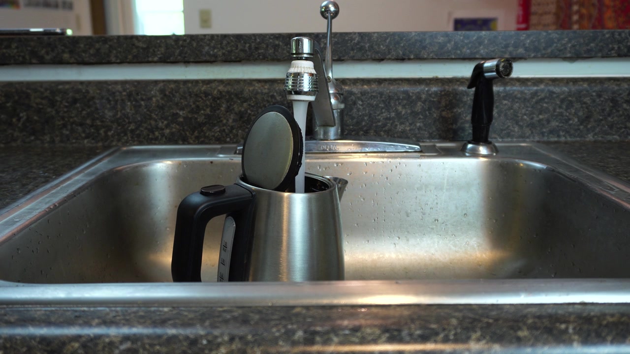 Primer plano de alguien llenando una tetera con agua del grifo para preparar café o té