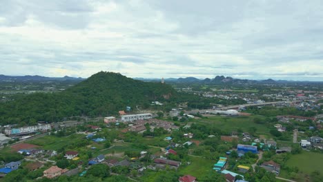 un dolly aéreo filmado sobre un paisaje verde y exuberante y edificios que se dirigen a la cima de la colina de khao kaen chan en la provincia de ratchaburi, tailandia