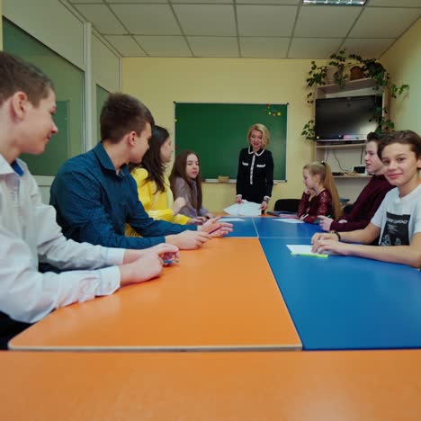 students raising hands in the classroom. teacher giving some tasks to children. teenage pupils sitting at one table during the lesson. concept of education.