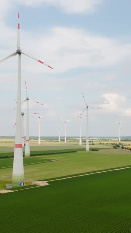 Vertical drone shot of a wind farm and traffic on a countryside road, summer day