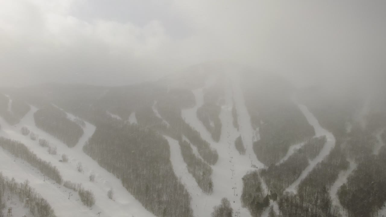 Snow-covered ski resort hidden in thick mountain fog, winter clouds scene, drone