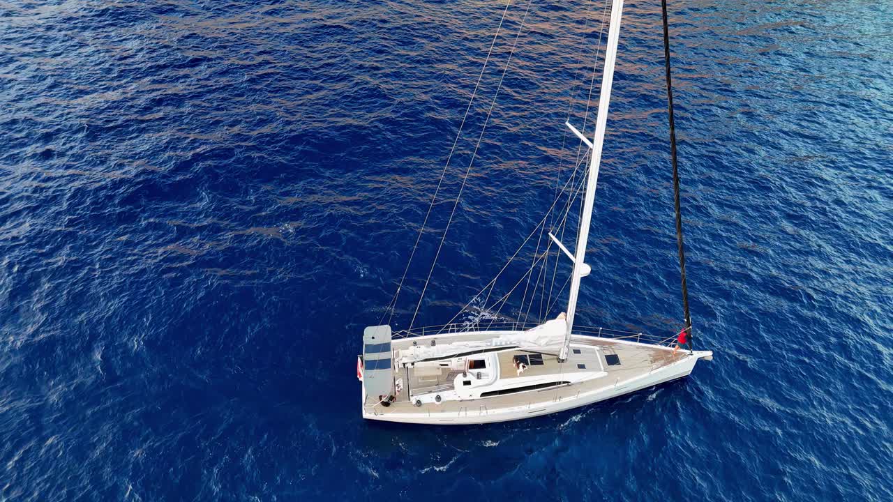 Vista aerea obliqua da drone di un elegante yacht a vela di lusso che scivola sulle acque blu profonde del Mediterraneo durante una giornata estiva soleggiata vicino alle scogliere frastagliate dell'isola di Gozo nell'arcipelago maltese