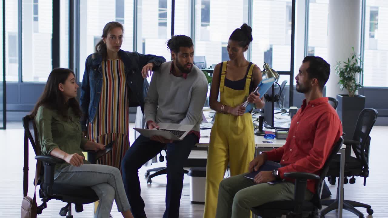 Gruppo eterogeneo di colleghi di lavoro che tengono in mano un laptop, un tablet e dei documenti, parlano e sorridono alla fotocamera