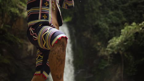 indigenous person playing kubing tribal instrument, behind is a waterfall while standing