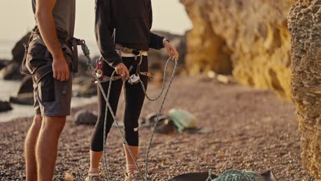 Shooting-close-up,-a-girl-in-a-black-sports-uniform-with-the-necessary-equipment-and-insurance-for-training-with-the-eye-trains-a-guy-and-tells-him-how-to-climb-a-rock-correctly.-Girl-rock-climber-trainer-tells-a-guy-how-to-climb-a-rock-correctly