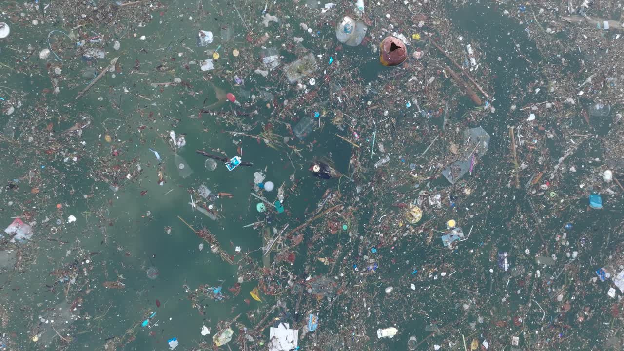 Low altitude top down drone shot of polluted water filled with trash floating over dead coral reef in the turqouise tropical water of Bali Indonesia