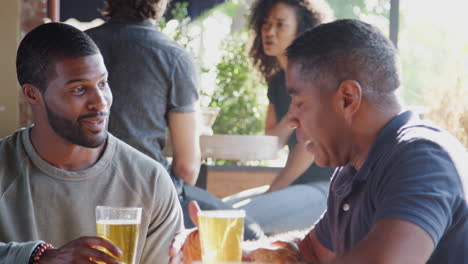 dos amigos se reúnen al aire libre en un bar deportivo disfrutando de una copa antes del juego