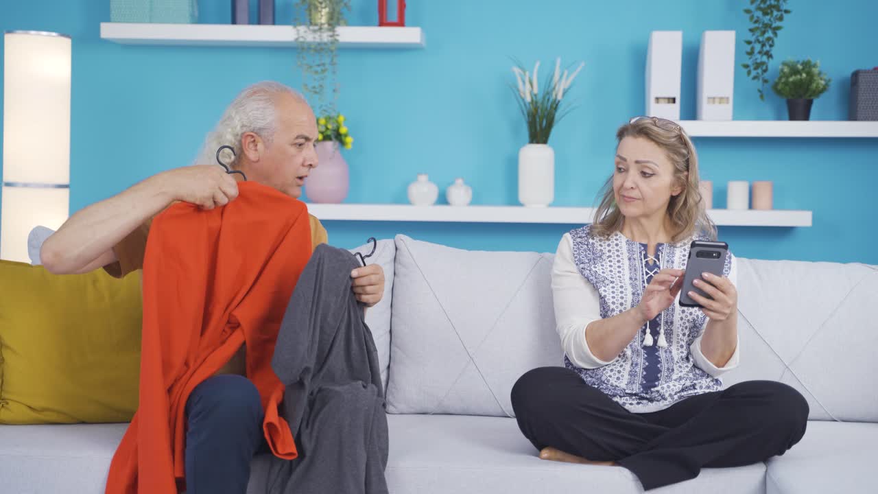 남자는 집에서 옷을 시도하고 그의 아내는 그를 도와줍니다.