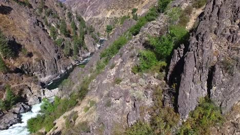 sliding shot of a steep and rugged canyon with a river and waterfall below