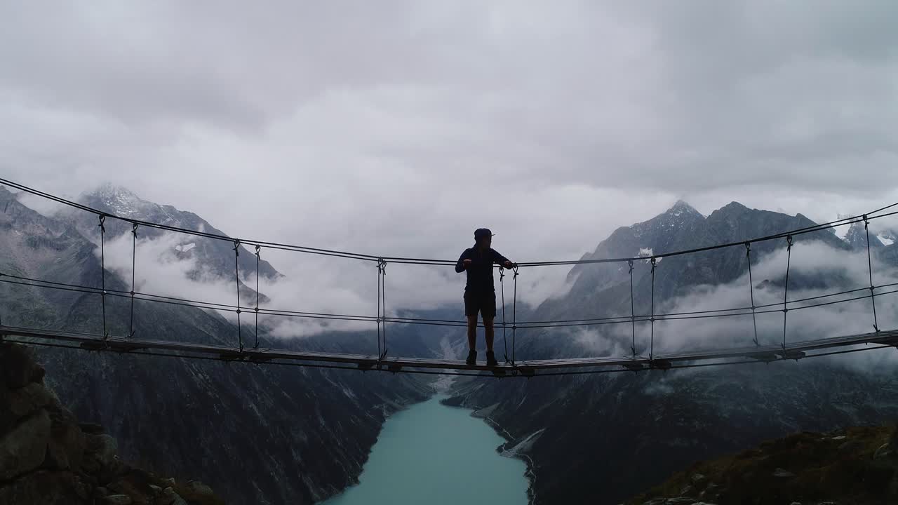 Thrilling slow motion shot of man jumping on narrow bridge above dramatic valley