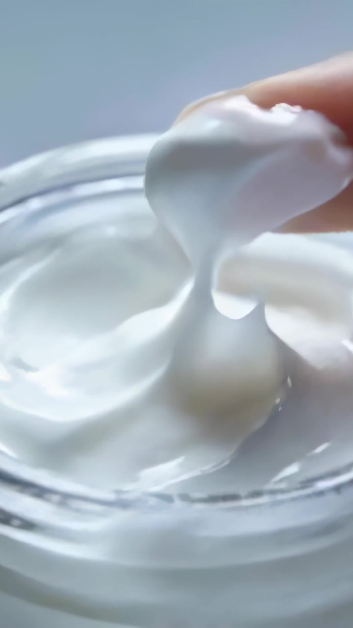 Video verticale: Premendo la punta del dito e poi sollevando crema densa da un barattolo di vetro su un tavolo, testandone la consistenza.