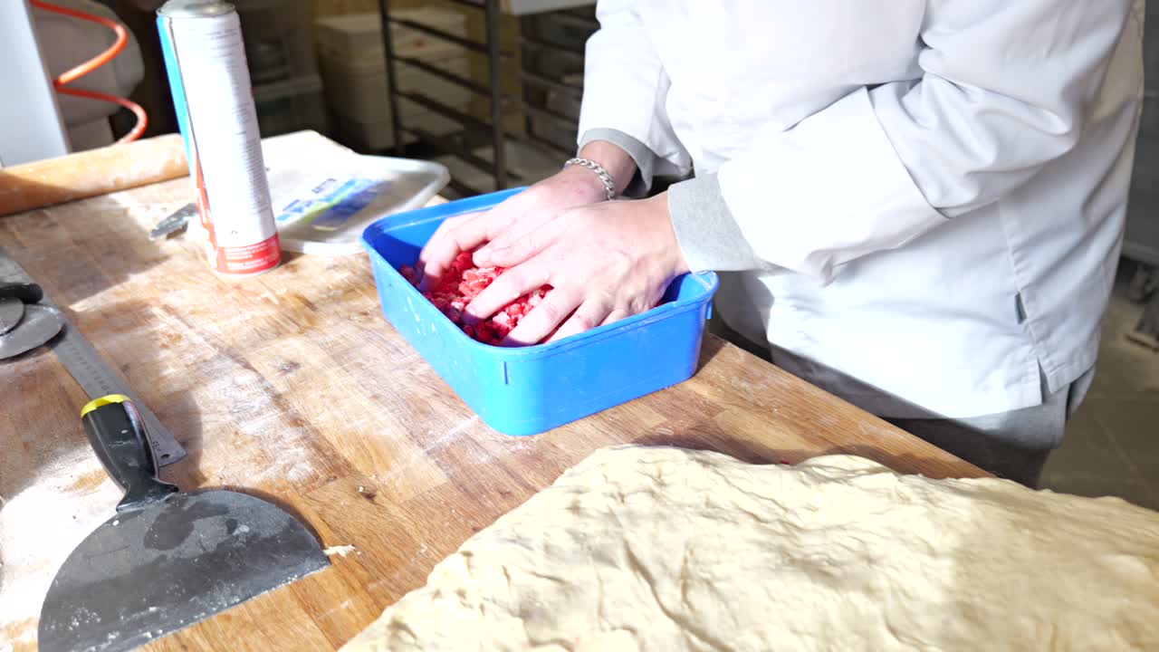 Ein Bäcker streut rosa Pralinen von Hand auf den ausgerollten Gebäckteig.