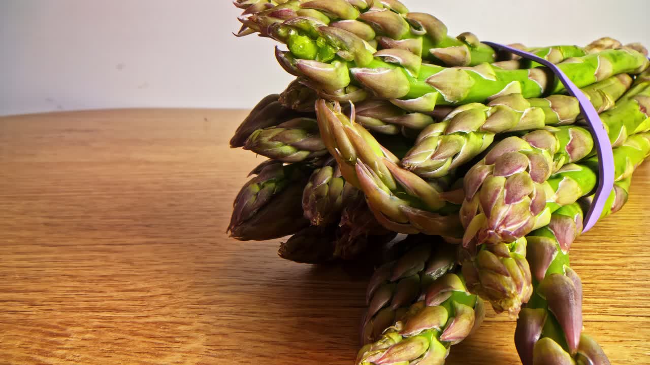 Bundle of green asparagus with rubber band on wooden kitchen table surface