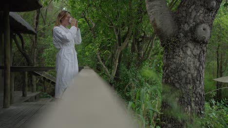 a woman drinking a morning coffee on the deck of a green outdoor garden