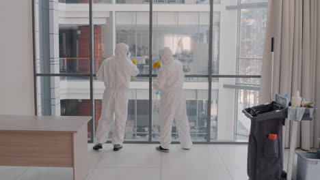 vista trasera de dos hombres de limpieza que usan equipo de protección personal limpiando paredes de cristal dentro de un edificio de oficinas