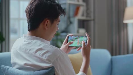 man playing game on smartphone while lying on sofa in the living room