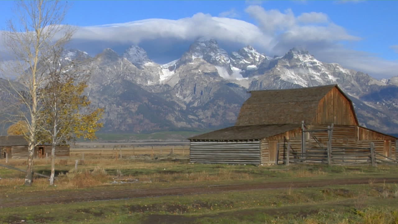 un antiguo granero se encuentra con las montañas grand teton al fondo