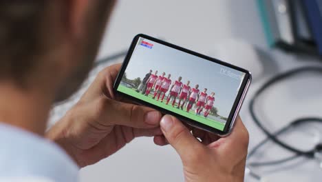 compuesto de un médico masculino viendo un evento deportivo en un teléfono inteligente