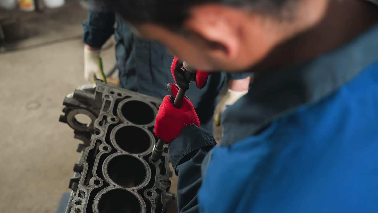 primer plano de la nuez de aflojamiento mecánica con guantes rojos mientras otro observador con guantes blancos se encuentra cerca en el taller, centrándose en el trabajo detallado del motor del automóvil