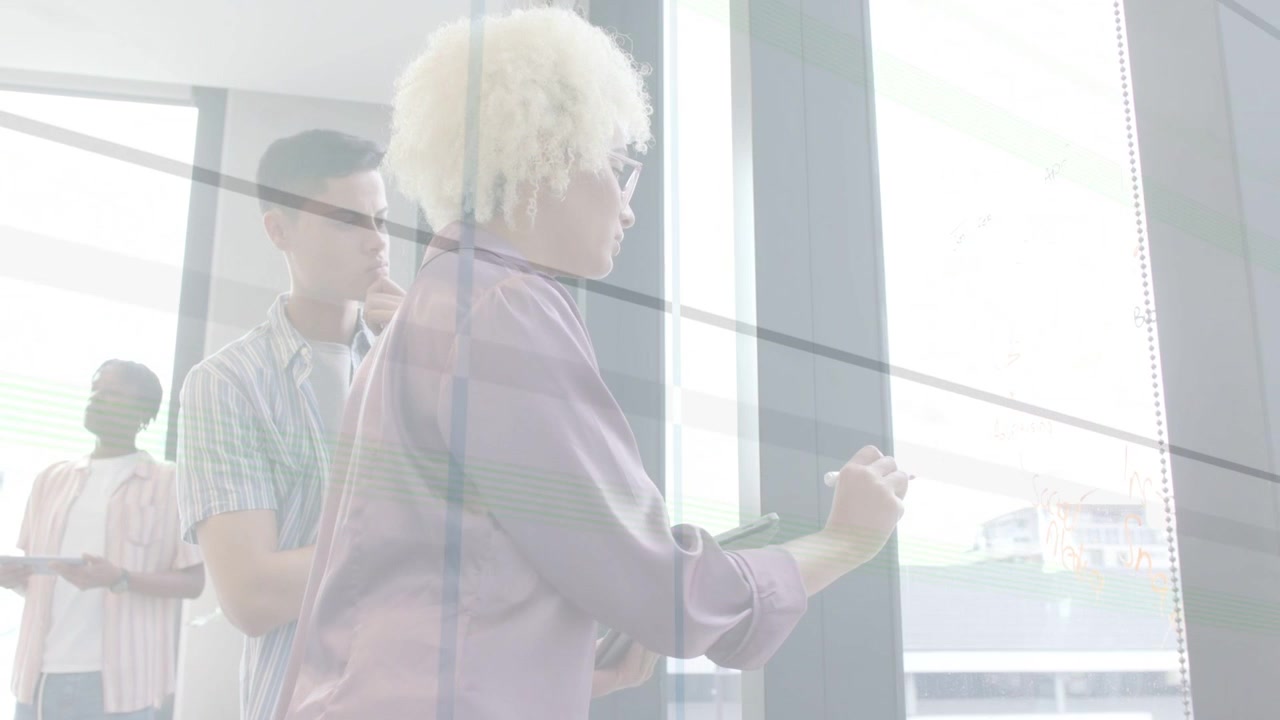 Facilitator stepping to glass, writing and animating business plan charts while teammate leaning in