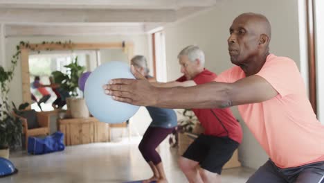 Focused-diverse-seniors-exercising-holding-balls-in-pilates-class,-unaltered,-in-slow-motion