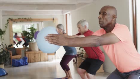 focused diverse seniors exercising holding balls in pilates class, unaltered, in slow motion