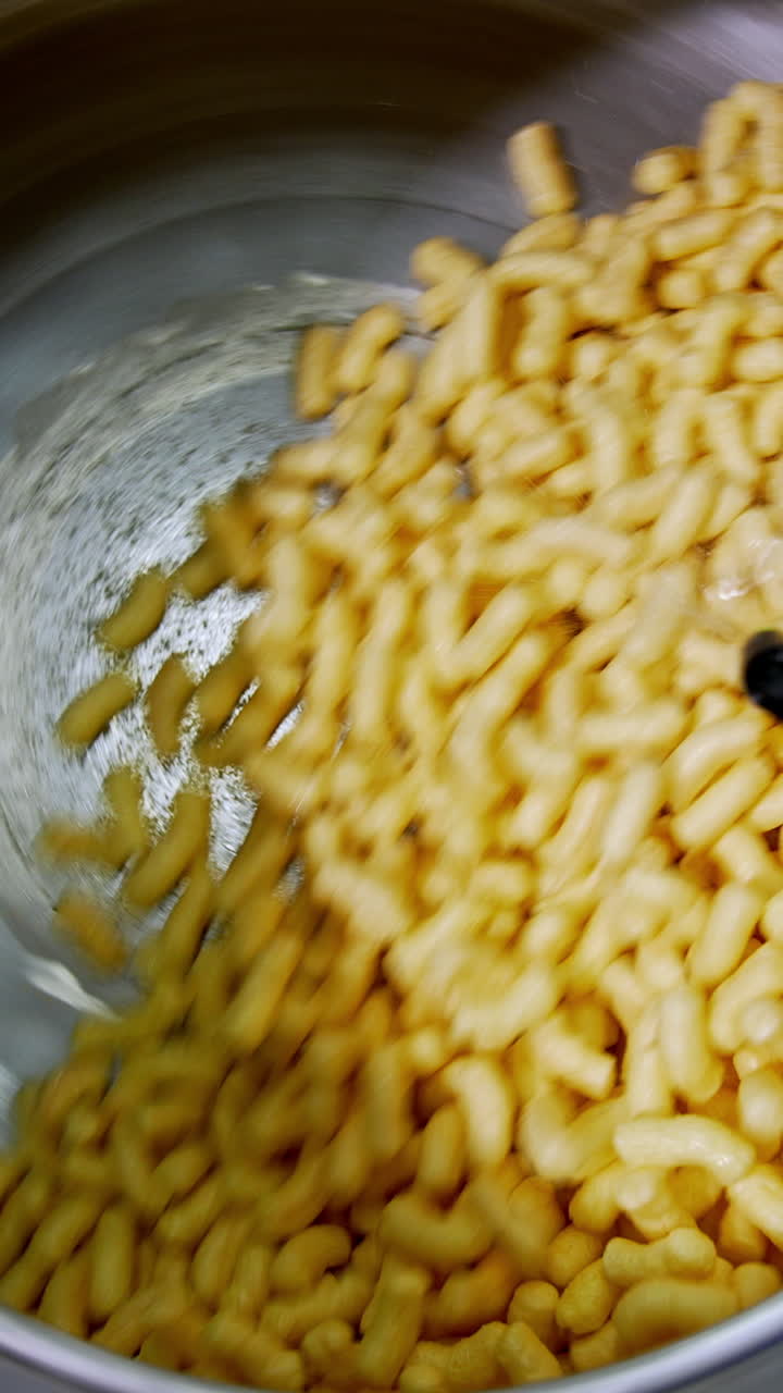 Corn sticks rotated in a metal tank being covered with sweet syrup. Snacks manufacturing close up. Vertical video