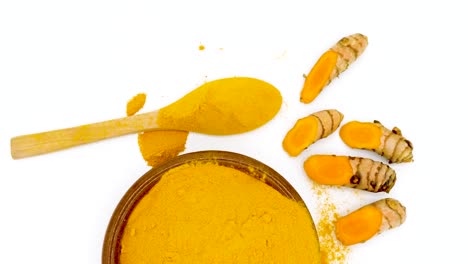 zoom out on a bowl with turmeric powder a wooden spoon and fresh turmeric