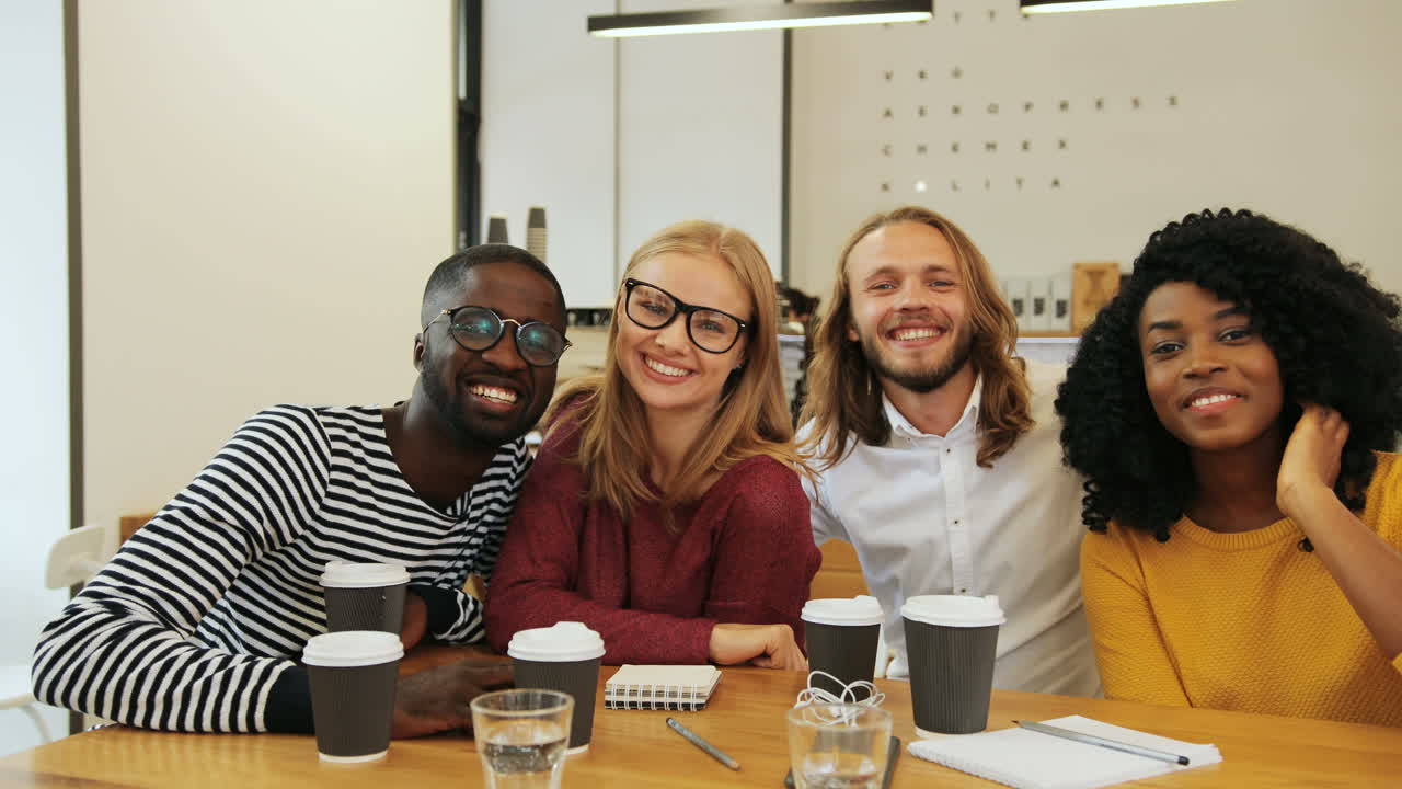 Multiethnic group of friends smiling and looking at camera sitting at a table in a cafe