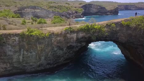 vuelo de vista aérea suave volar hacia adelante en un agujero en un dron de roca disparó playa rota en penida en bali