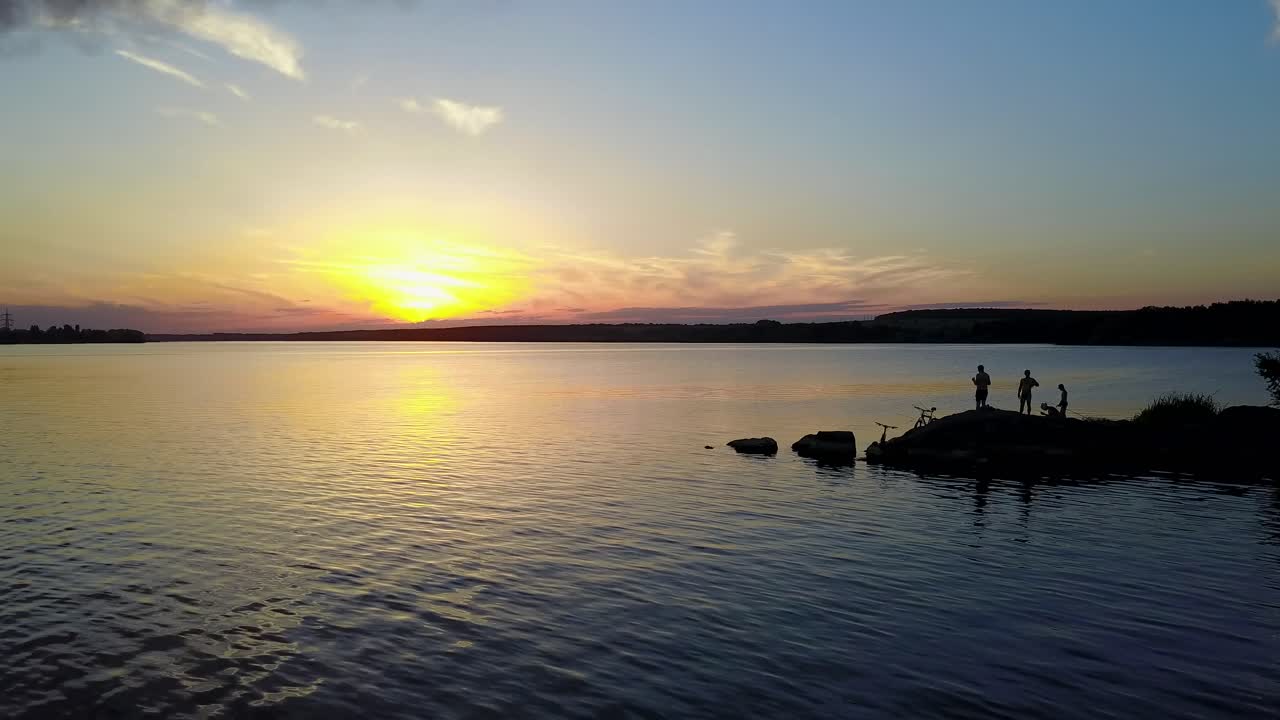 Persone che si rilassano sulla riva di un fiume, godendosi il tramonto sul fiume