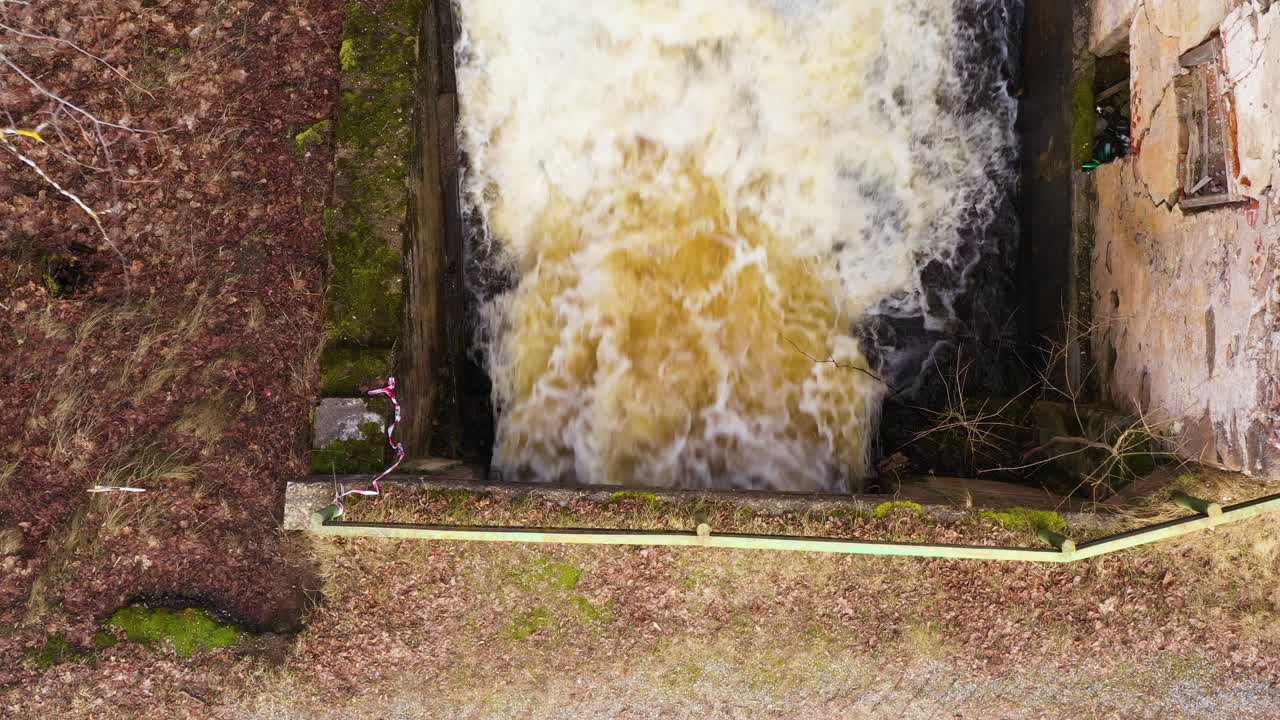 Powerful man made waterfall near abandoned millhouse building, aerial top down view