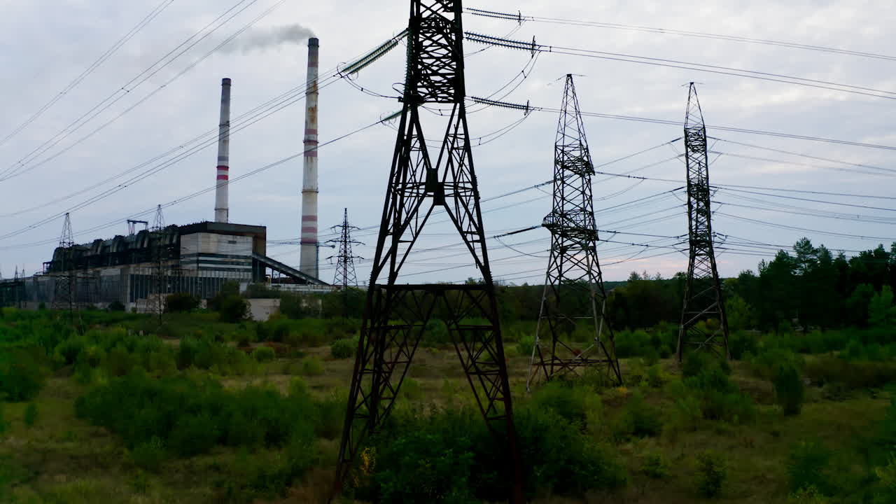 High-voltage electric tower. Transmission lines on the background of industrial factory. Steel power pylons on field in the countryside. Camera rising up.