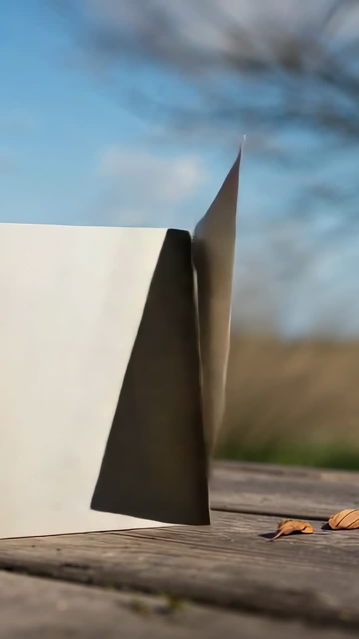 Vertikales Video: Leichter Wind stupst eine leere, cremefarbene Karte an, die auf einem Holztisch steht und sich neigt, Blätter, Platz für Text
