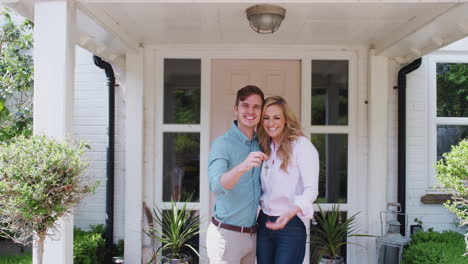 Portrait-Of-Couple-Holding-Keys-To-New-Home-Standing-Outside-Front-Door