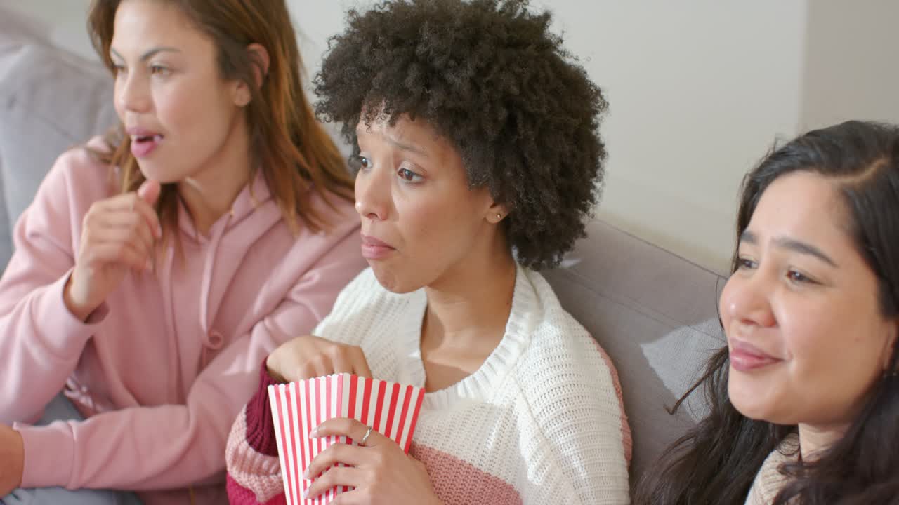 Forskellige veninder reagerer på en filmscene i sofaen derhjemme, gisper og spiser popcorn fra spande.