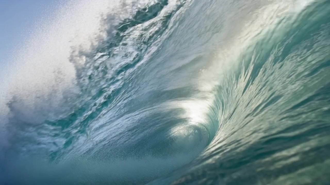 Forming from incoming swell, hollow-barrel wave toward shore, curling lip with sunlit glints, foam