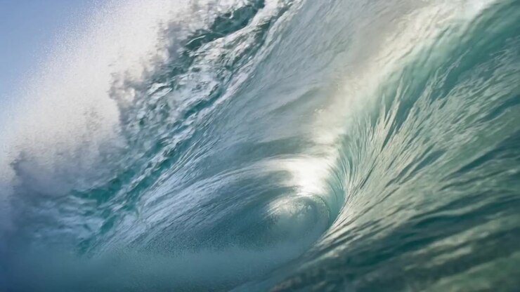 Forming from incoming swell, hollow-barrel wave toward shore, curling lip with sunlit glints, foam
