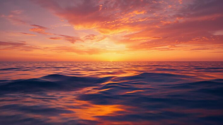 Sun descending below horizon causing clouds, waves reflecting gold and purple hues across open sea