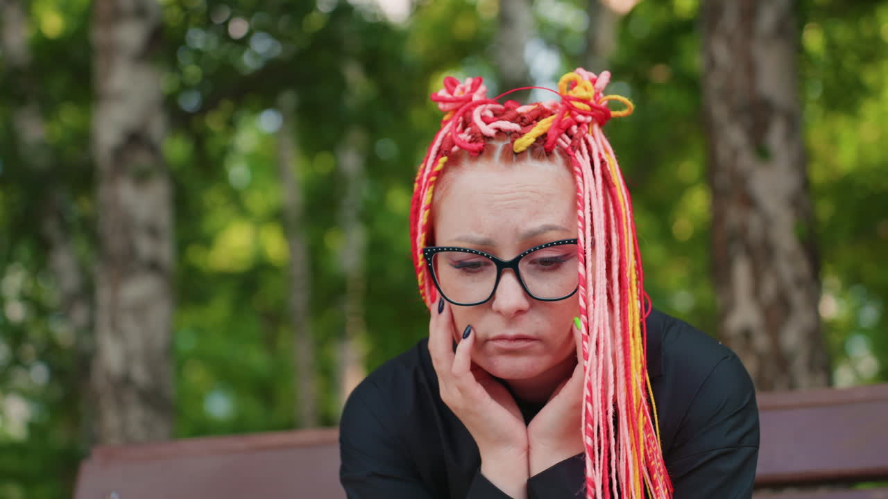 고요한 공원에서 사색에 잠긴 채, 평화로운 순간을 즐기는 여성의 모습입니다. 생기 넘치는 머리카락과 생각에 잠긴 표정으로 벤치에 앉아 잎이 무성한 주변 환경을 감상하며 사색에 잠겨 있어요.