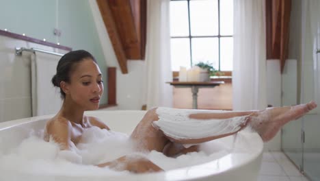 mixed race woman taking a bath shaving her legs