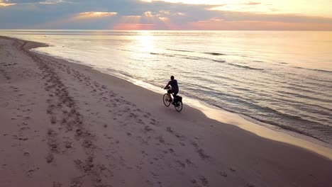 toma aérea en cámara lenta de un joven montando en bicicleta en la playa al atardecer