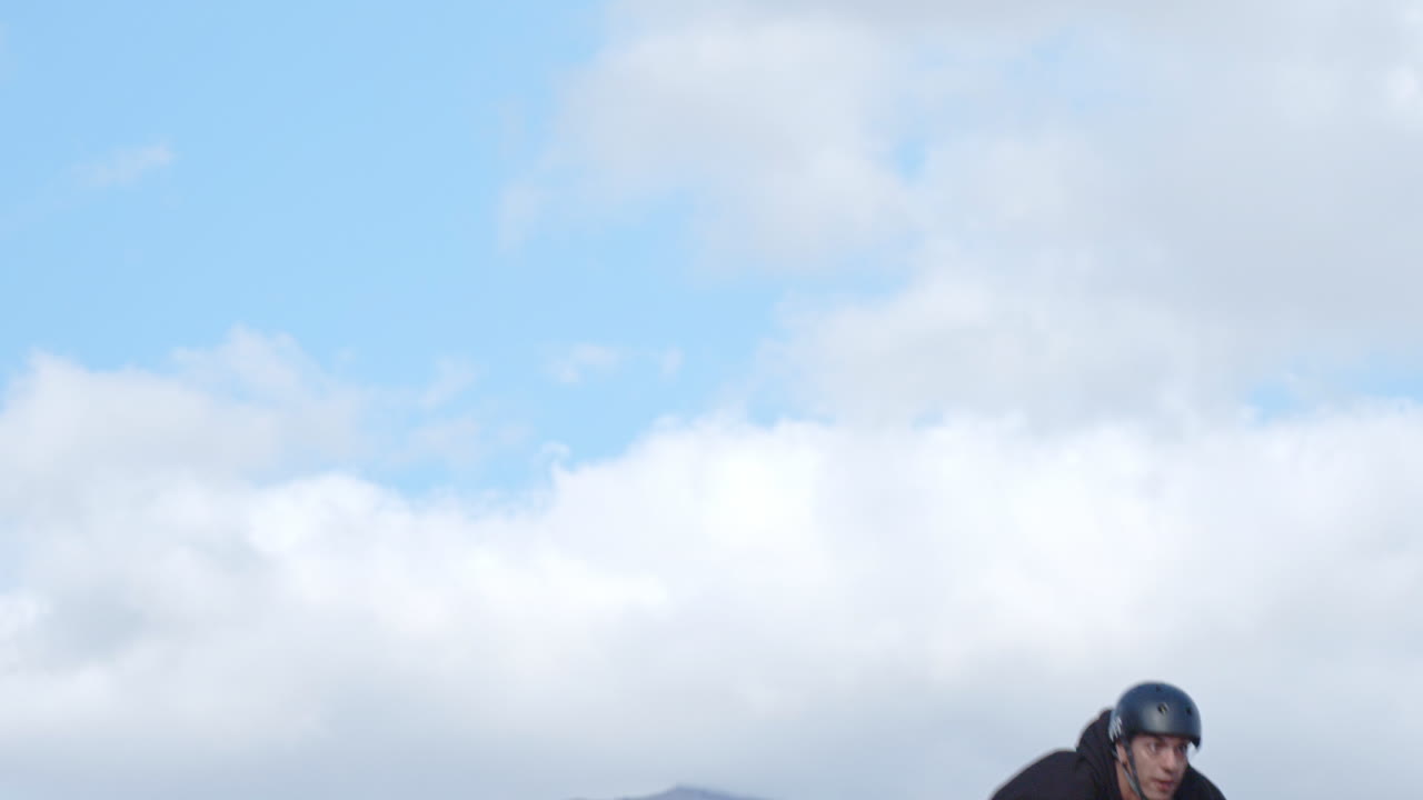 Extreme Sport Mountain Biking. A young man on a bike dirt jumping in slow motion.  Blue sky and scattered clouds in the background.