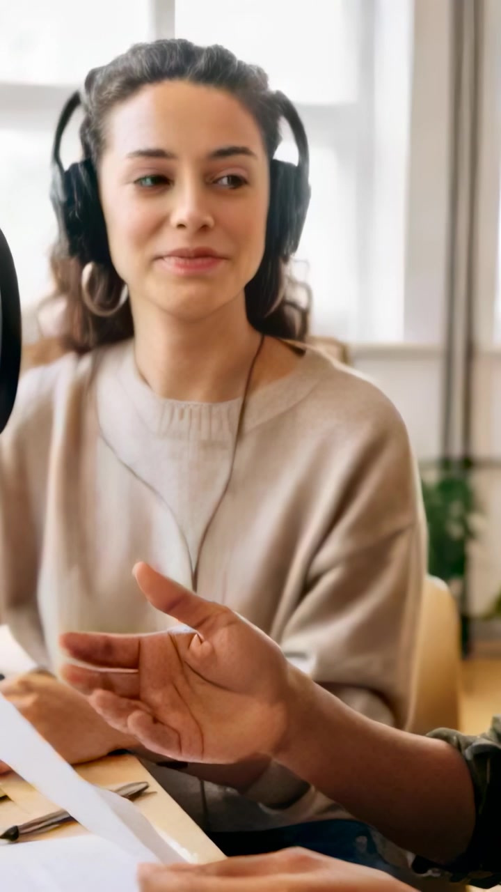 Vertical video: Leaning as hand entering script, host with headset and hoops reading and nodding