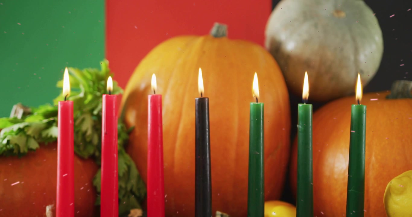Camera holding closeup on kinara showing seven lit candles flickering over split red-green backdrop